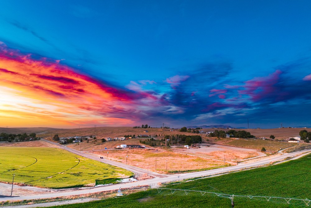 An aerial view of green farm fields, country roads, and homes in the Idaho countryside under a colorful sunset sky.